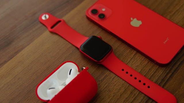 Red smartphone, AirPods, and smartwatch placed on a table, showcasing wearable tech and audio accessories.