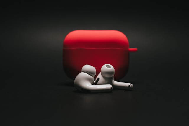 Red AirPods case with white AirPods placed in front, showcasing wireless audio accessories.
