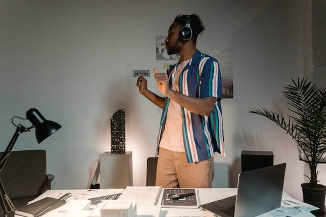 Man standing in a tech office listening to music with headphones, enjoying a modern workspace environment.